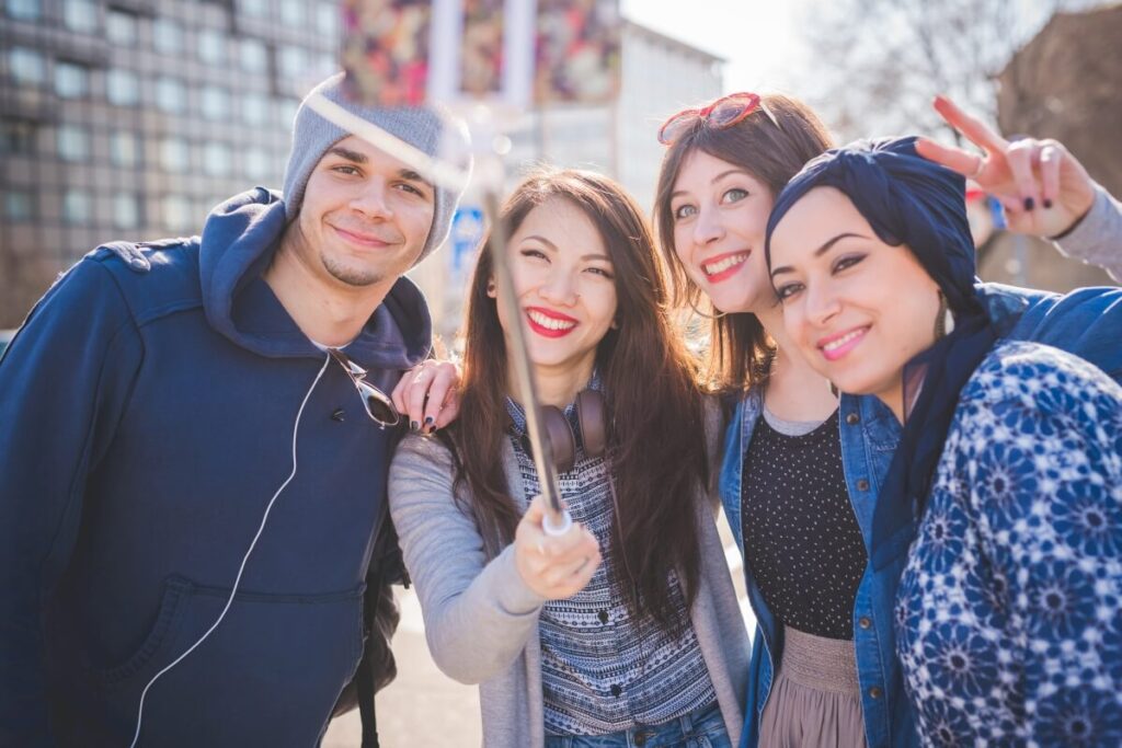 Grupa uśmiechniętych ludzi robi sobie selfie na świeżym powietrzu, promując legalizację pobytu cudzoziemców.