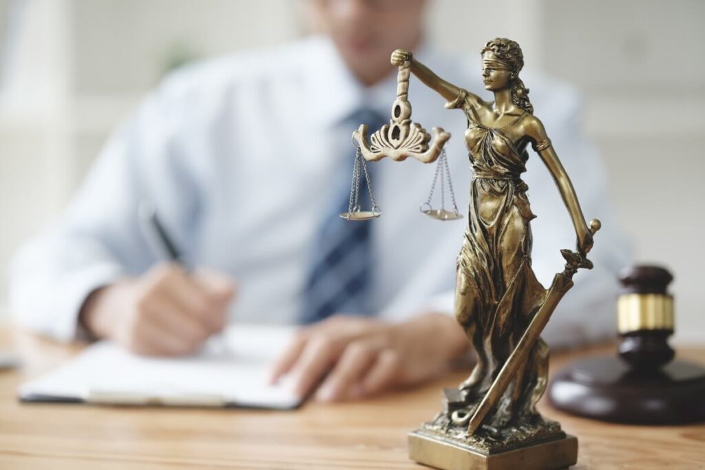 Statua Temidy na biurku prawnika podczas pracy nad dokumentem dotyczącym prawa spadkowego.