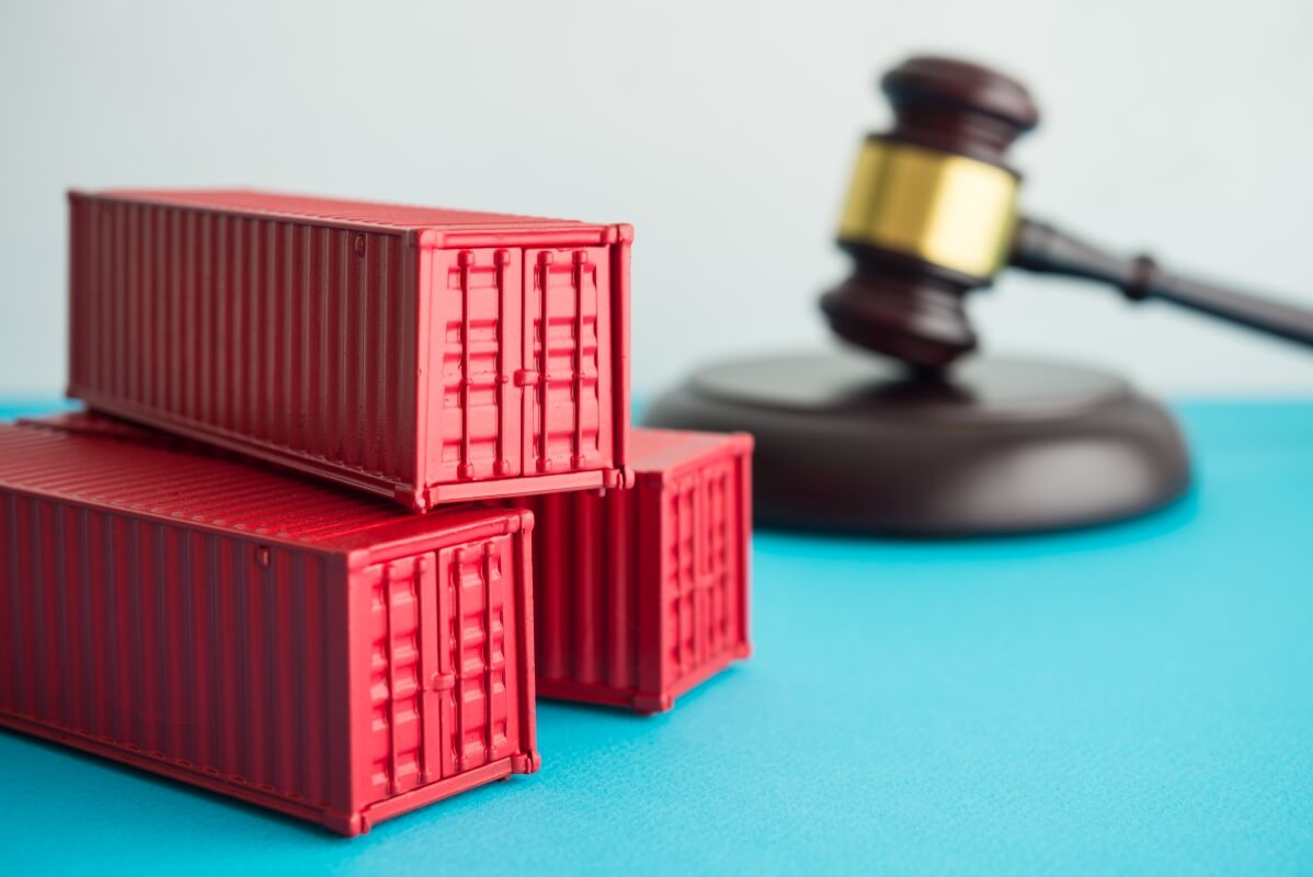 Czerwone kontenery i sędziowski młotek symbolizujące prawo transportowe.
