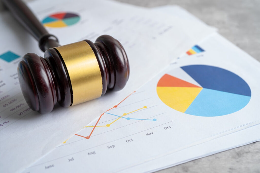 Młotek sędziowski leży na wykresach dotyczących prawa gospodarczego.
