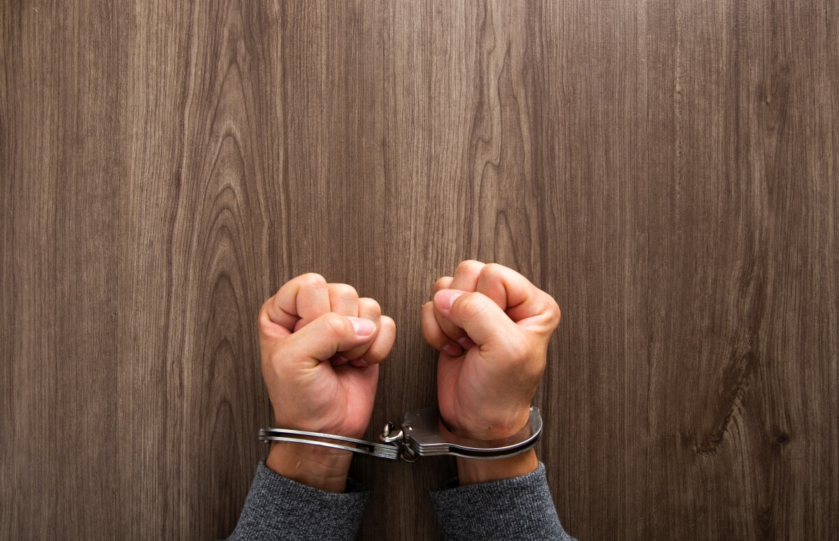 Zaciśnięte dłonie w kajdankach nawiązują do tematu, jakim jest prawo karne wykonawcze.